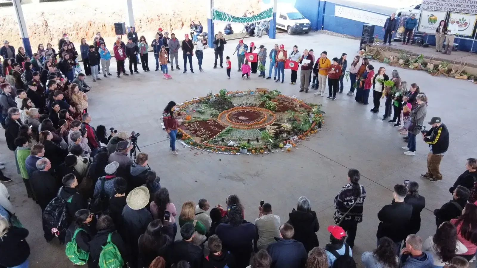 Roda de pessoas em volta de uma mística com sementes e flores no chão de um ginásio