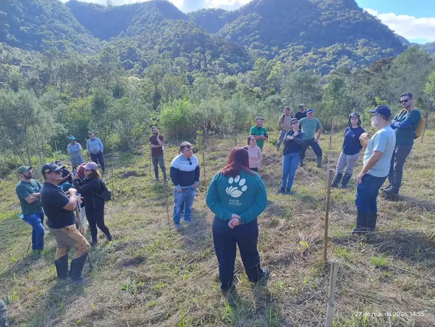 Grupo reunido em um campo com mudas plantadas e morros ao fundo